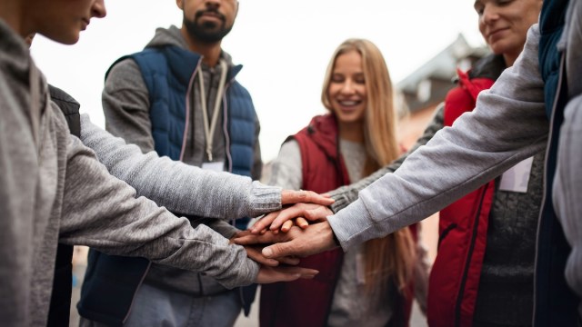 Babbel Social Impact team represented by a group of people all putting their hands in the center of a circle while standing outside.